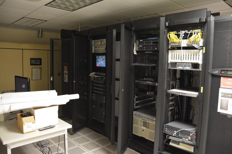 A data center server hall with rows of equipment racks under blue light